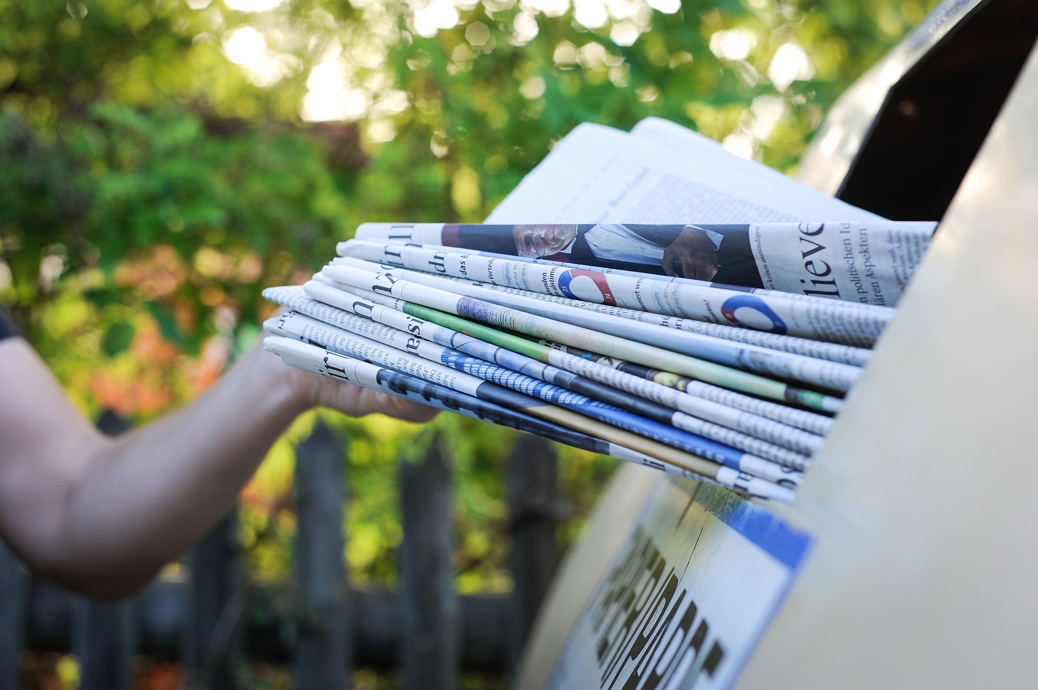 Person wirft Papier in einen Recycling Container
