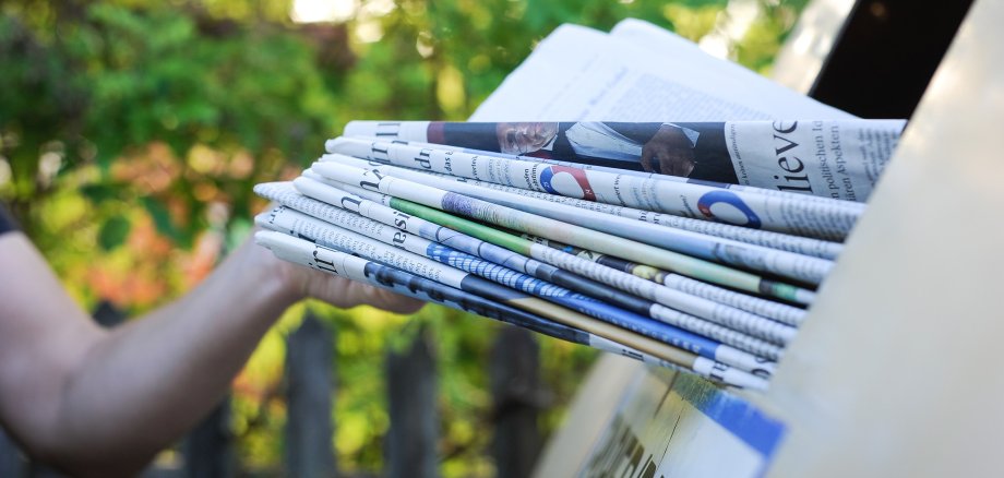 Person wirft Papier in einen Recycling Container