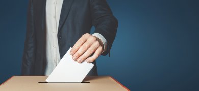 Unrecognizable male voter holds in his hand a ballot above the ballot box Unrecognizable male voter holds in his hand a ballot above the ballot box