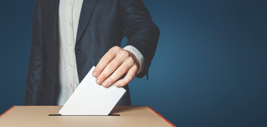 Unrecognizable male voter holds in his hand a ballot above the ballot box