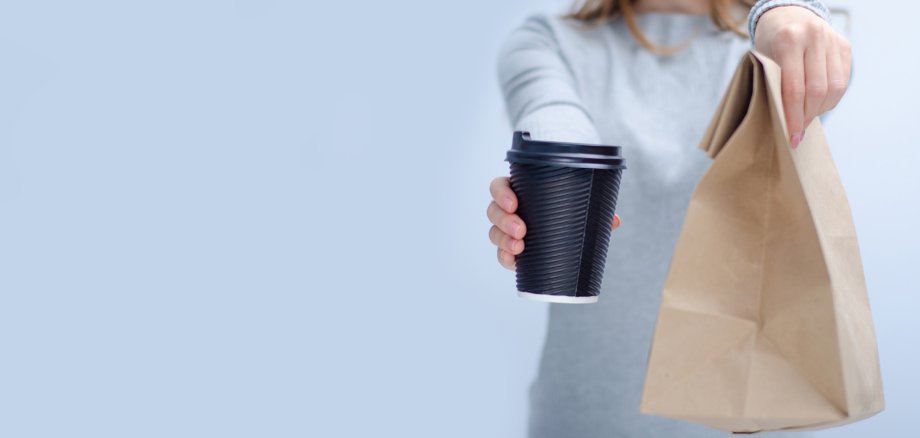 Woman holding cardboard cup of coffee and package food take and go in hand