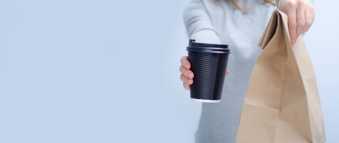 Woman holding cardboard cup of coffee and package food take and go in hand